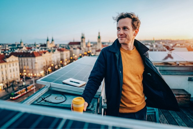 Mann steht auf Dachterrasse und blickt auf die Stadt, daneben Panele